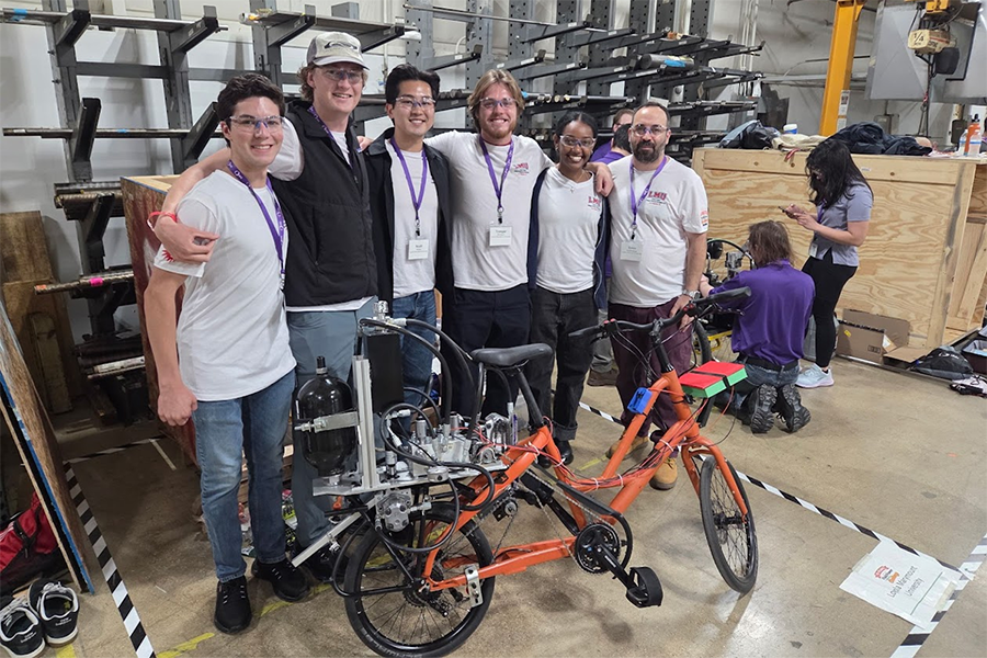 mechanical engineering students standing behind fluid powered vehicle they created